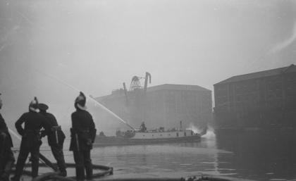 Surrey Docks: Firemen fighting a fire in South Dock on 8th March, 1936. A fire float monitor directs a jet of water from the middle of the basin. By A.G. Linney. Museum of London 2012.28/261